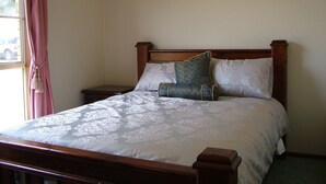 A neatly made bed with a floral bedspread and two pillows, a wooden headboard, a nightstand, and a framed picture on the wall. - Halls on Falls Homestead (Strath Creek)