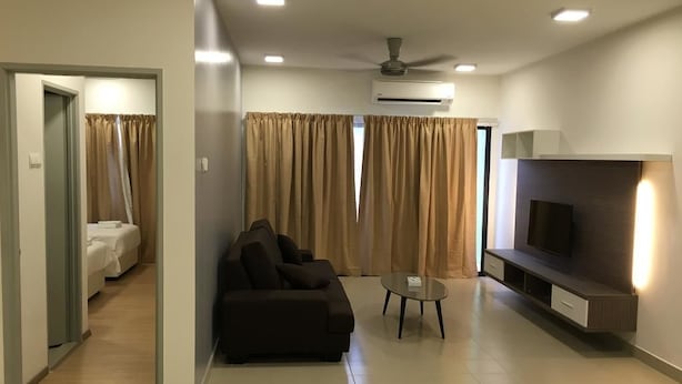 A modern living room with a sofa, a coffee table, and a TV mounted on the wall. There is a door leading to a bedroom with a bed. - Alami Garden Hotel (Shah Alam)