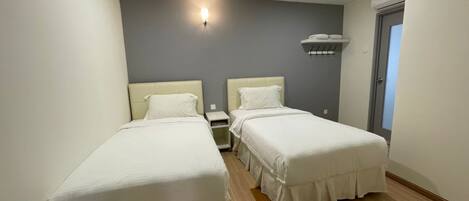 A hotel room with two single beds, a small bedside table, a wall-mounted light, and a window with a view.