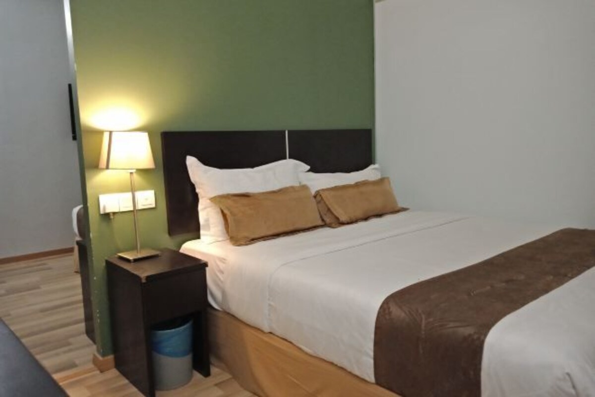 A neatly made bed with white and brown bedding, a bedside lamp, and a small wooden nightstand with a trash bin.