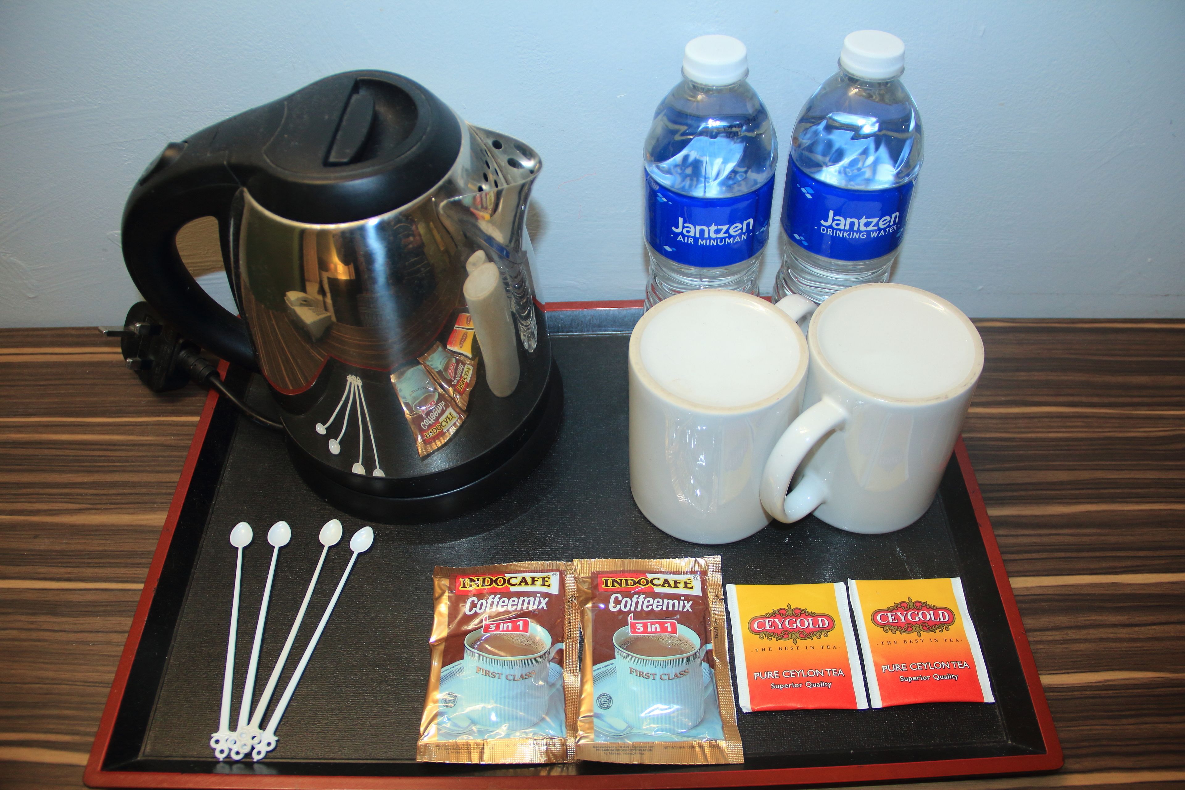 Un plateau contenant une cafetière, deux bouteilles d’eau, deux tasses, des sachets de thé et un ensemble de cuillères.