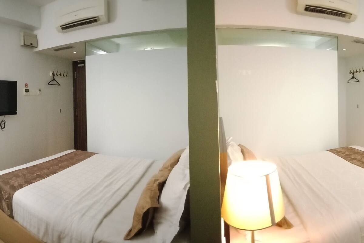 A mirrored room with two beds, a TV on each wall, and a lamp between them.