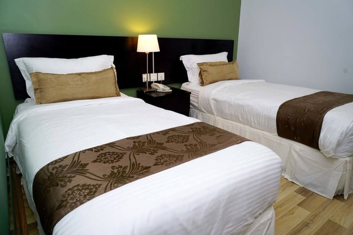 A hotel room with two beds, each with white linens and brown decorative pillows. There is a nightstand with a lamp and a phone between the beds.