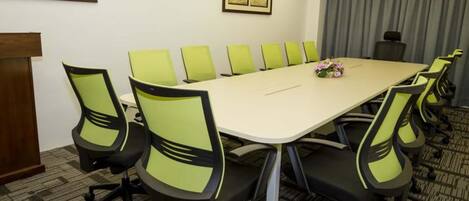 A conference room with a long table and green chairs, a podium, and framed artwork on the walls.