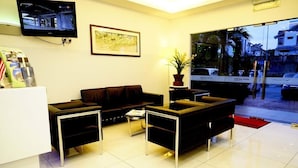 A modern reception area with a sofa set, a TV mounted on the wall, and a framed picture. - Alami Garden Hotel (Shah Alam)