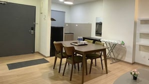A modern dining area with a wooden table and chairs, a small round table with a flower, and a kitchen in the background. - Alami Garden Hotel (Shah Alam)