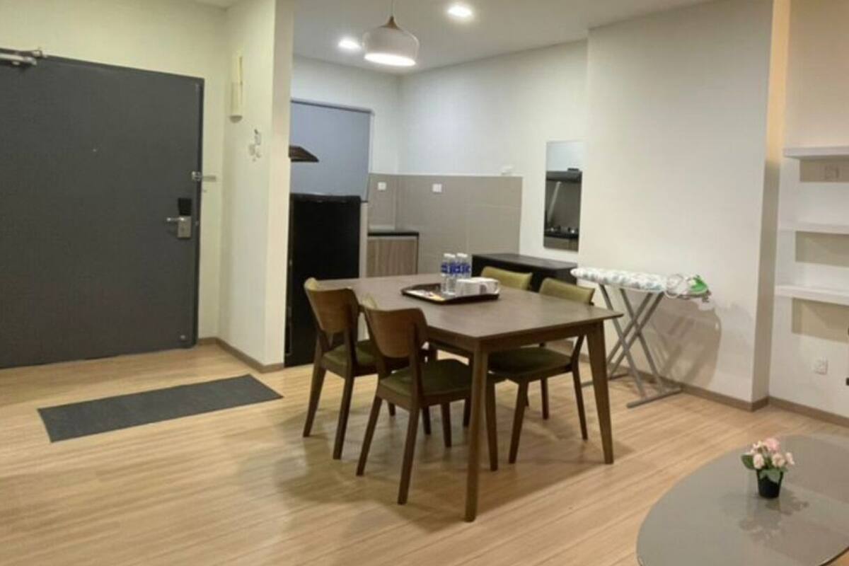 A modern dining area with a wooden table and chairs, a small round table with a flower, and a kitchen in the background.