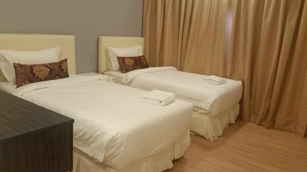 Une chambre d’hôtel avec deux lits, chacun agrémenté de draps blancs et d’oreillers décoratifs. La chambre est dotée d’un plancher en bois et de rideaux beiges.