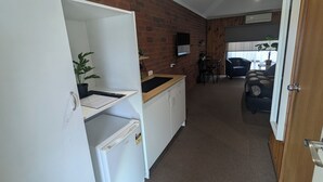 A compact kitchen with a refrigerator, a sink, and a countertop. There is a dining area with a table and chairs, and a sofa in the background.