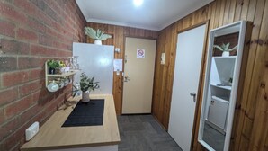 A compact kitchen with a brick wall, wooden paneling, a white refrigerator, and a small shelf with plants and kitchenware.