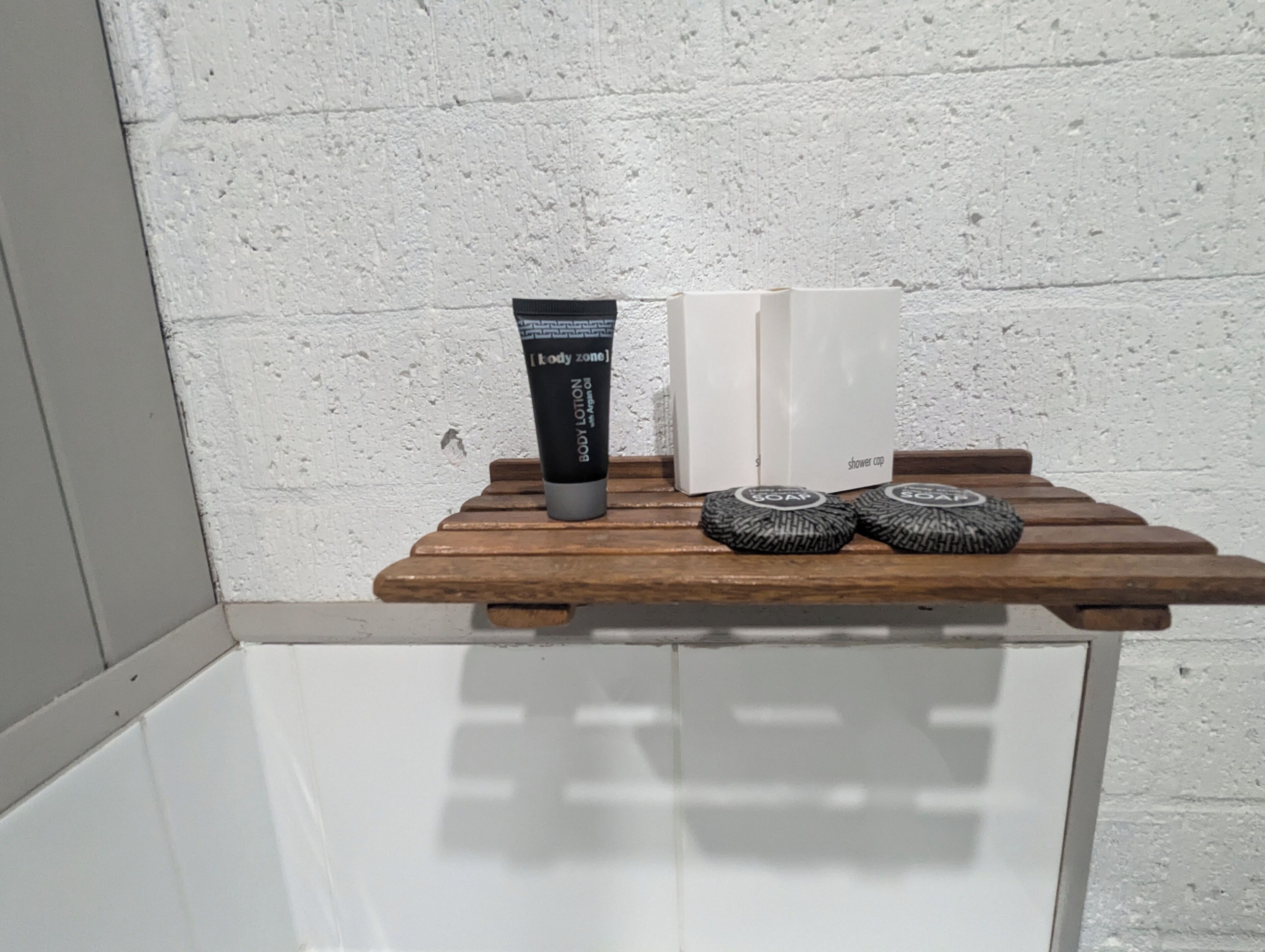 A wooden shelf with a body lotion tube, a shower cap, and a soap bar.