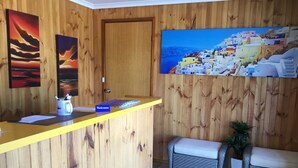 A reception area with a wooden wall, a reception desk, a 'Welcome' sign, a painting of a coastal village, and a bench.