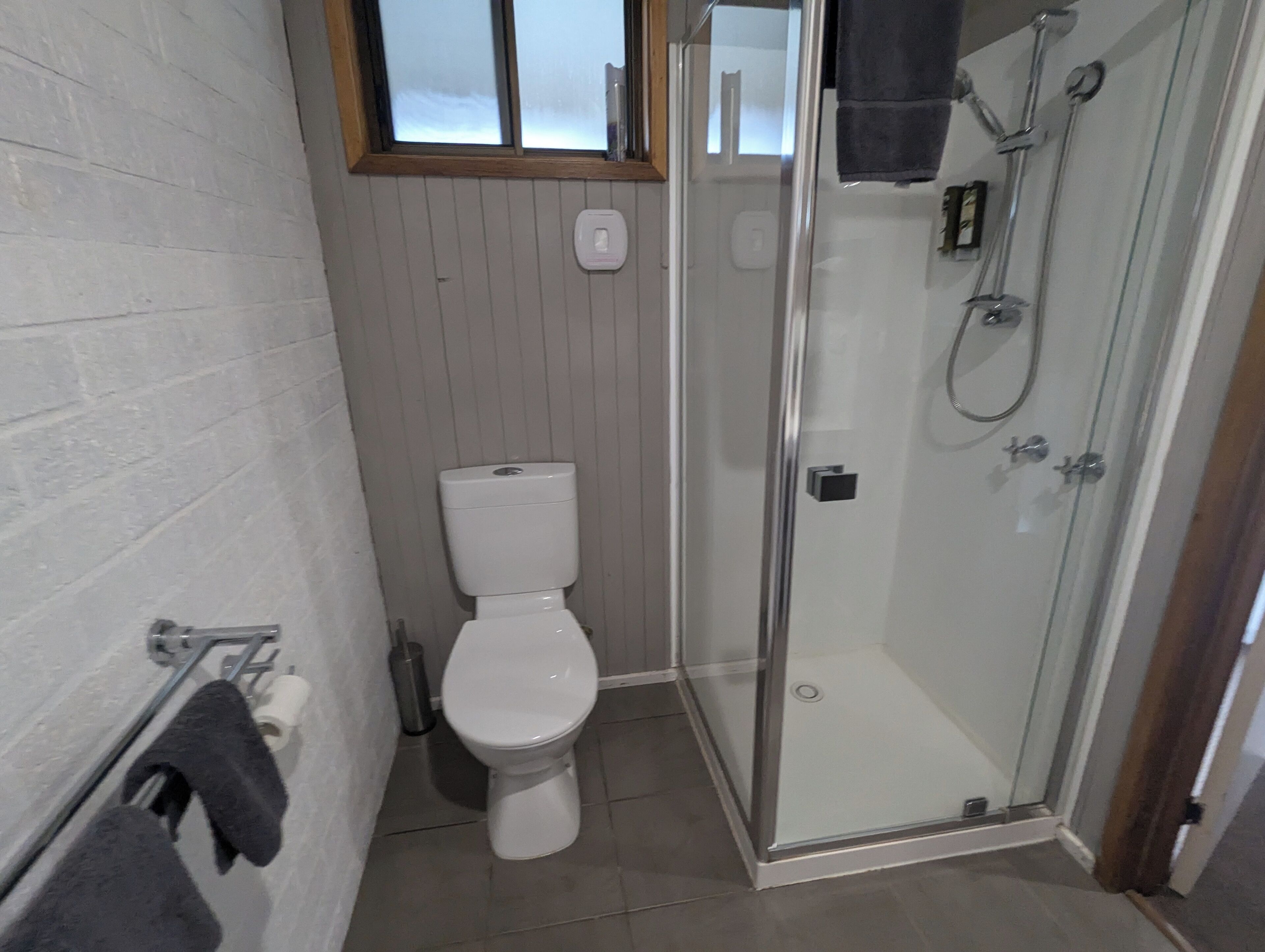 Un baño con inodoro, ducha con mampara de vidrio y un perchero para toallas.