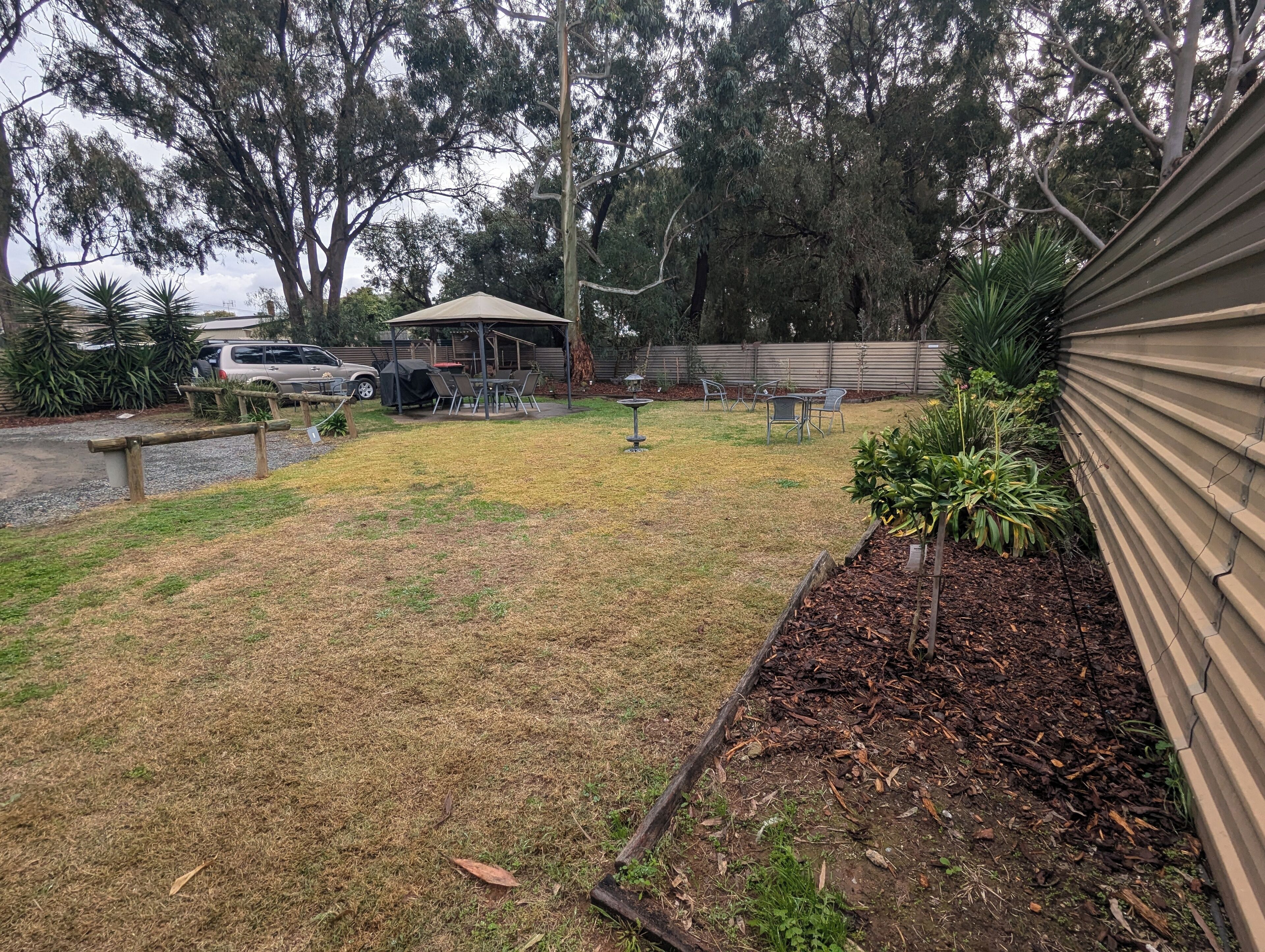 A backyard with a covered patio, a barbecue grill, and a car parked nearby.