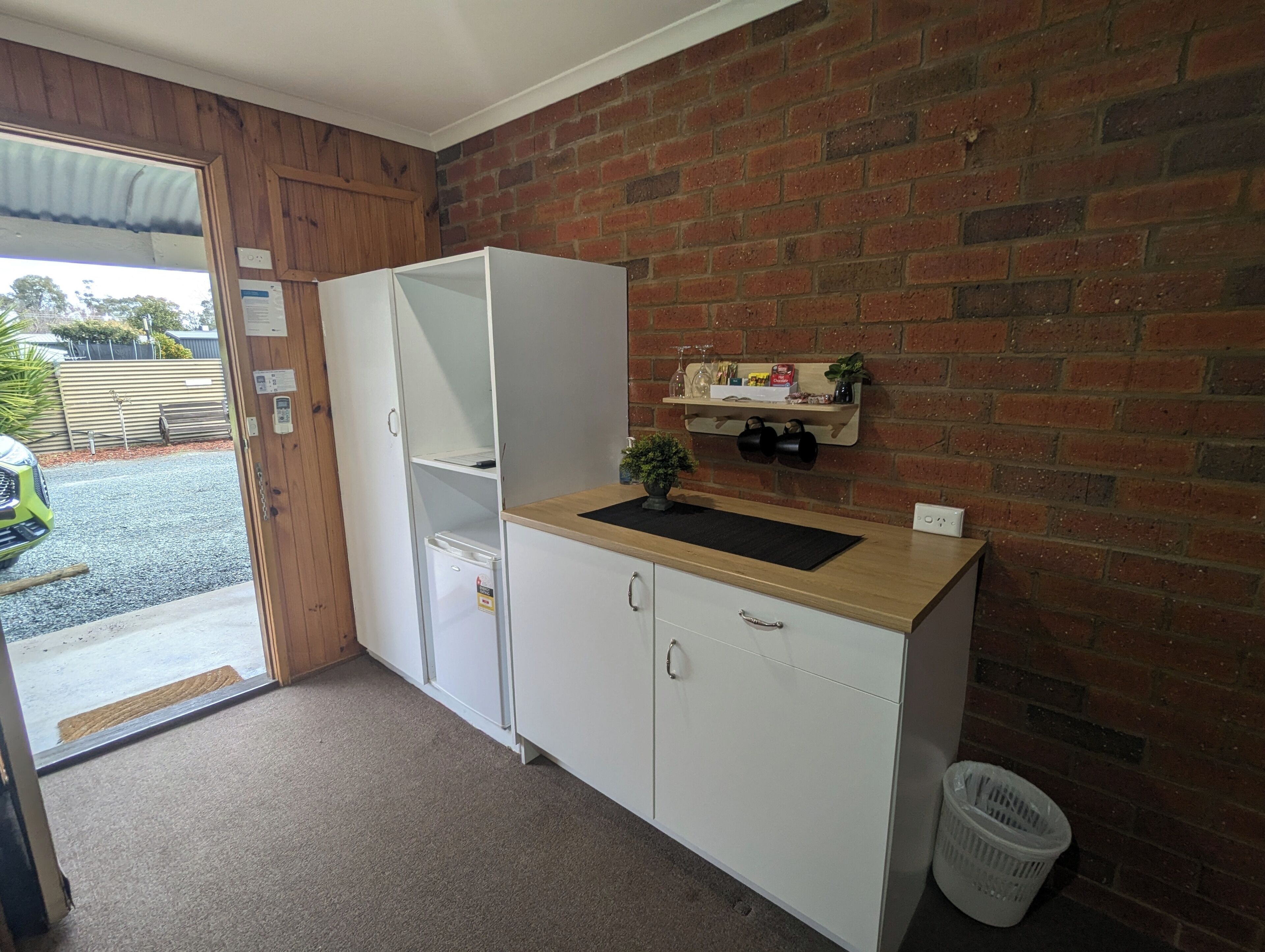 A compact kitchen with a white fridge, a wooden countertop, and a brick wall.