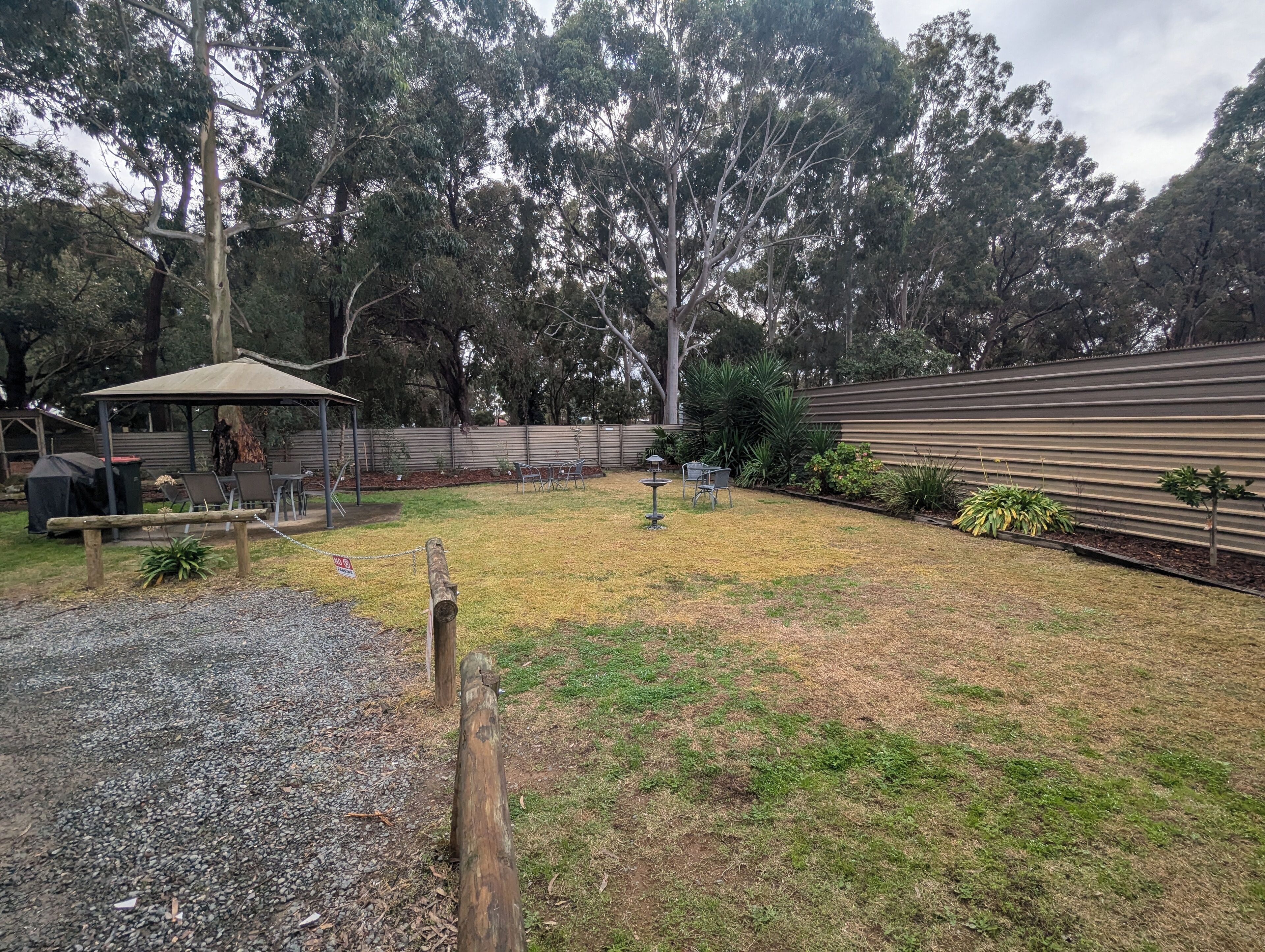Patio trasero con zona de estar techada, una parrilla y un área de juegos cercada.