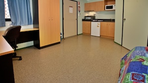 A compact room with a desk, a bed, a kitchenette, and a door. - Karratha Lodge (Karratha Industrial Estate)