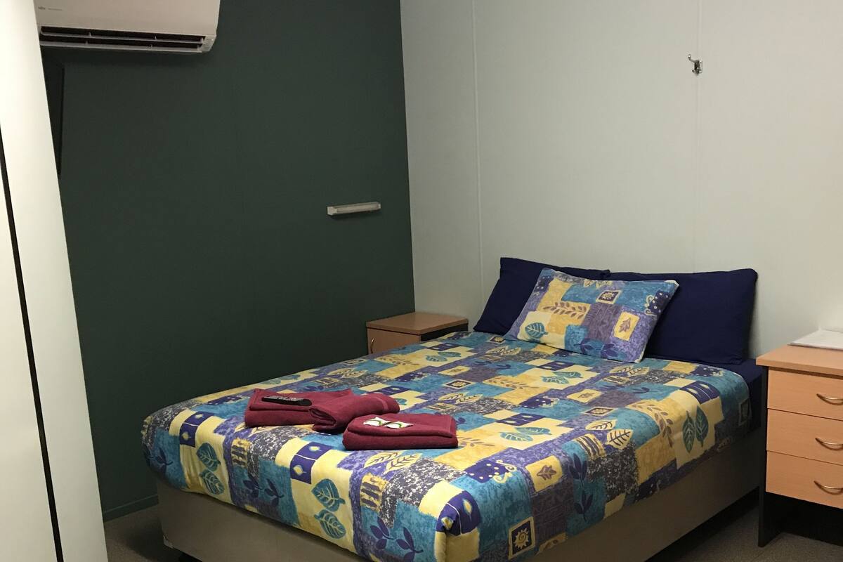 A bedroom with a bed, a nightstand, a dresser, and an air conditioning unit.
