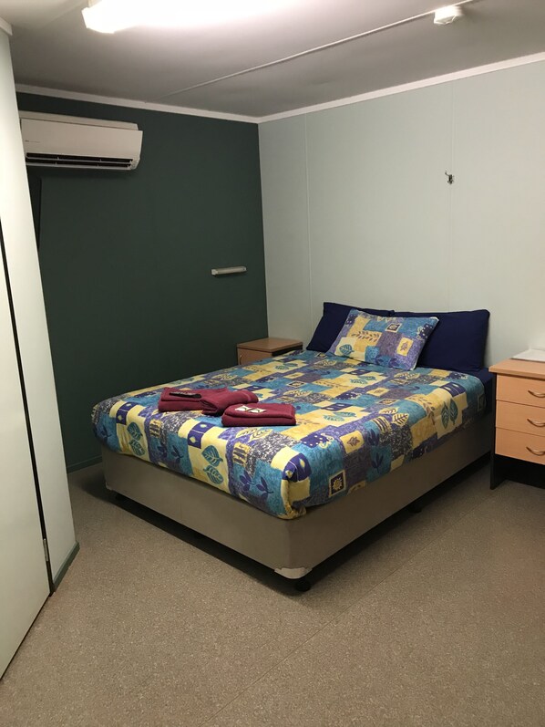 A bedroom with a bed, a nightstand, a dresser, and an air conditioning unit. - Karratha Lodge (Karratha Industrial Estate)
