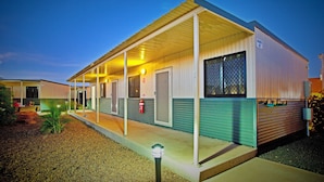 A single-story building with a covered porch, a fire extinguisher mounted on the wall, and a small garden area with gravel and plants. - Karratha Lodge (Karratha Industrial Estate)