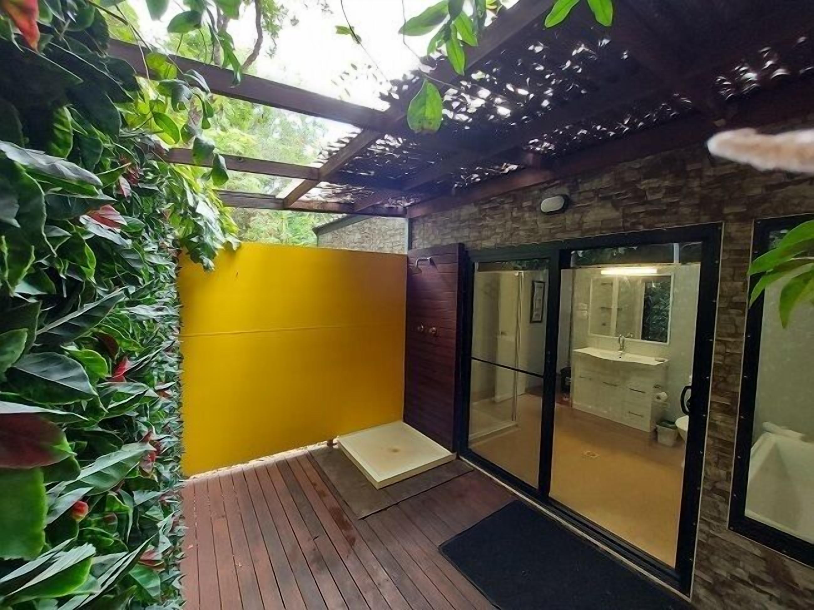 Ein Badezimmer mit Glastür, gelber Wand und Holzterrasse.