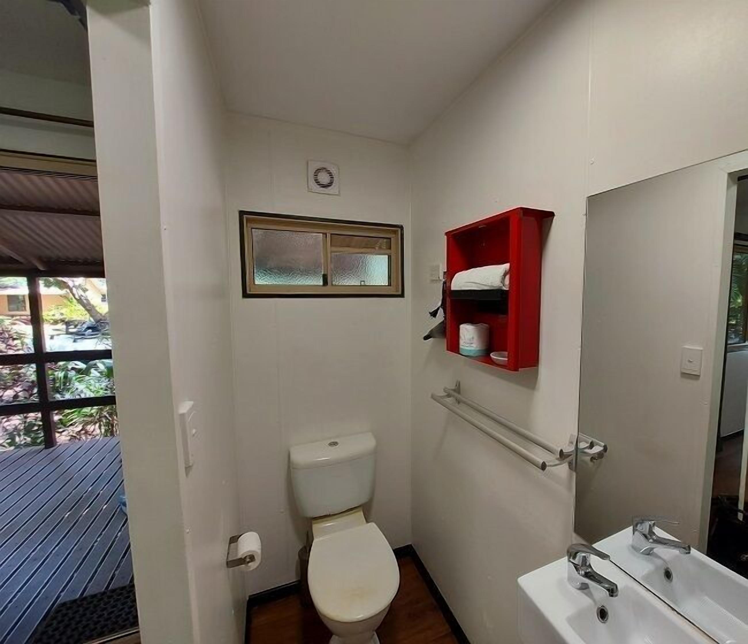 A small bathroom with a toilet, a sink, a red medicine cabinet, and a window above the toilet.