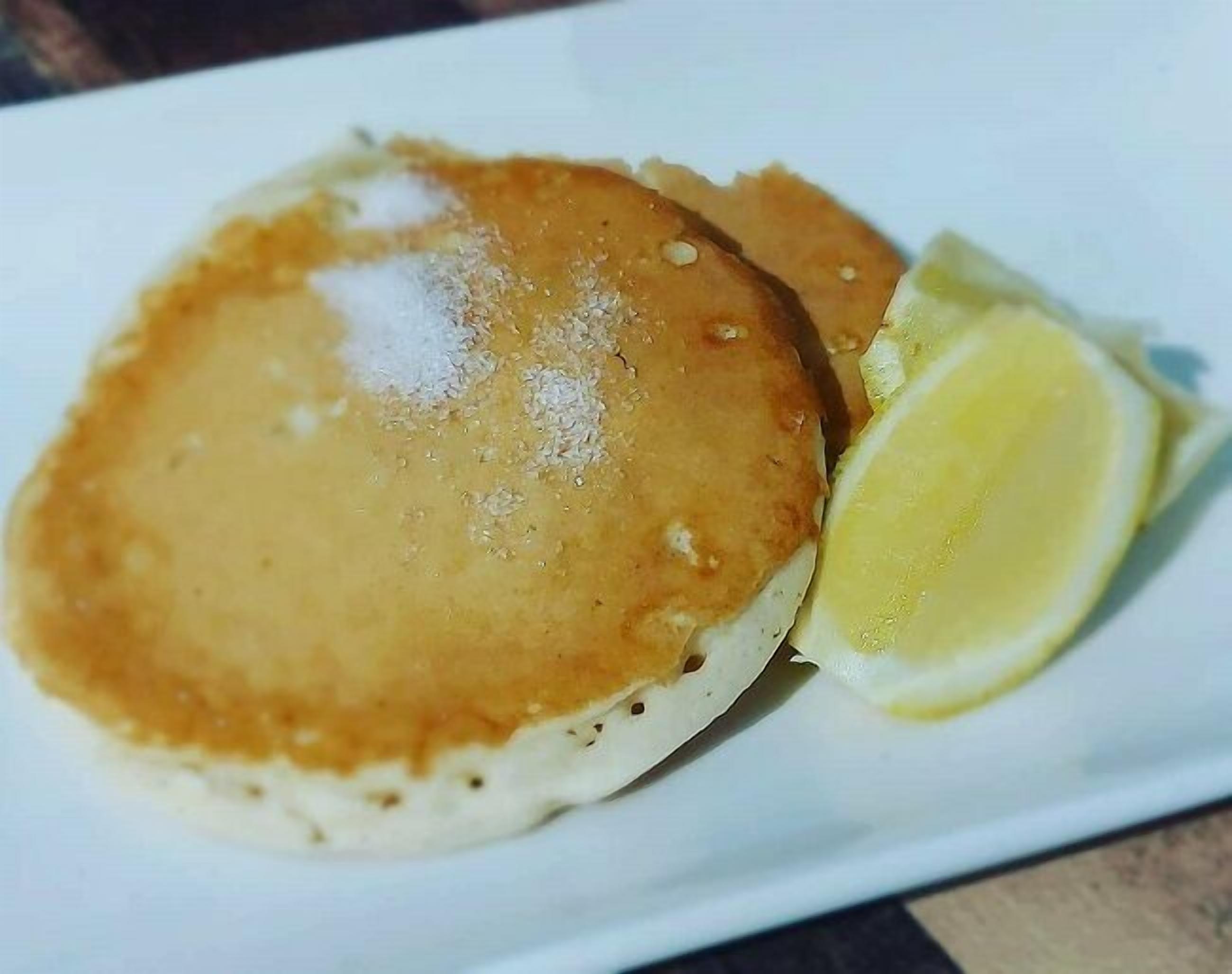 Un plato con dos tortitas y un gajo de limón.