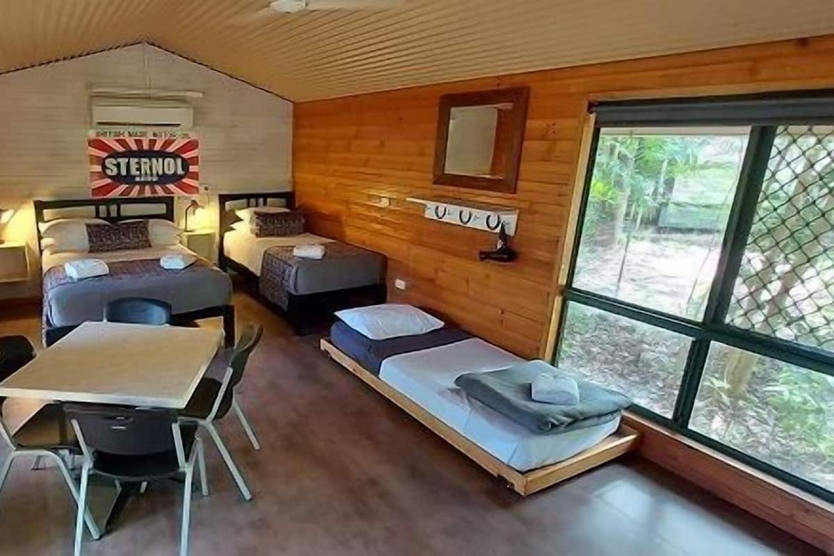 A cozy cabin-style room with two beds, a dining table, and a large window.