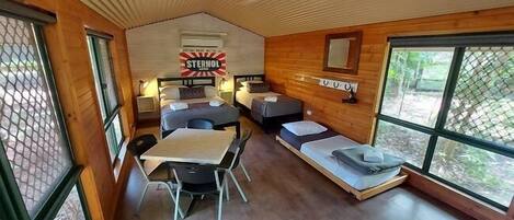 A cozy cabin-style room with two beds, a dining table, and a large window.