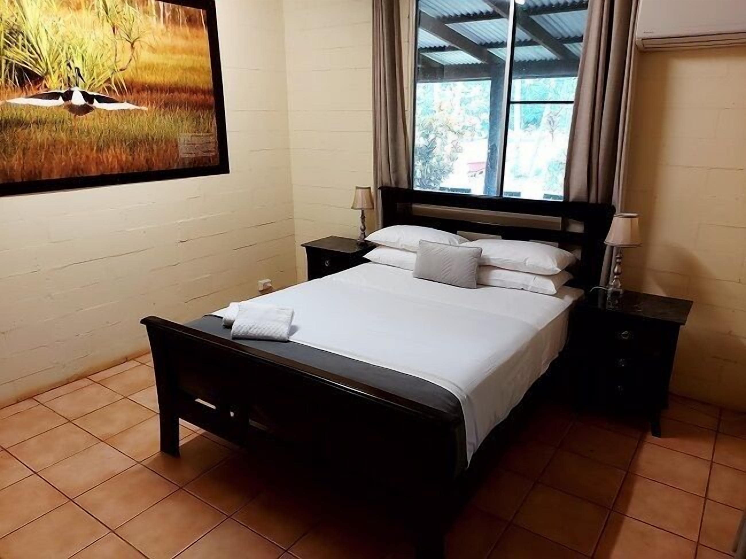 A neatly made bed with white linens and pillows, a wooden headboard, and two bedside tables with lamps.