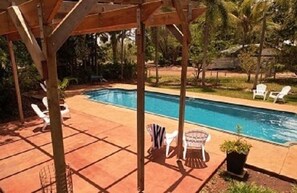 A rectangular pool with a wooden pergola overhead, surrounded by a tiled patio.