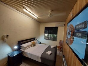 A bedroom with a bed, bedside table, lamp, window, and a wall-mounted TV displaying a sign.