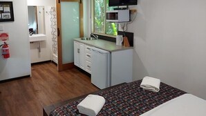 Een compacte hotelkamer met kitchenette, een bed met een bedspread met patroon, en een kleine badkamer.