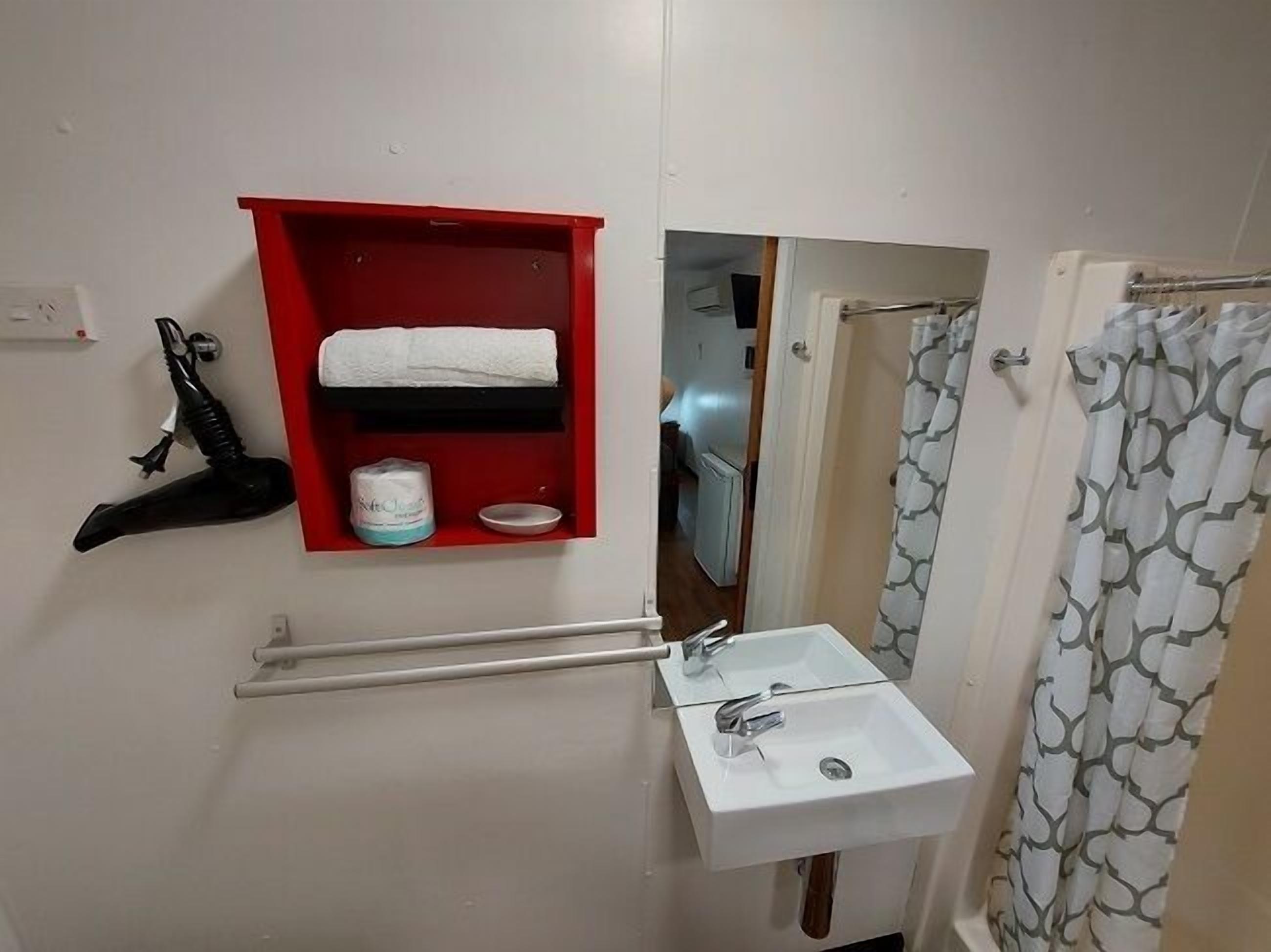 A bathroom with a white sink, a red medicine cabinet, a black hairdryer, and a shower curtain.