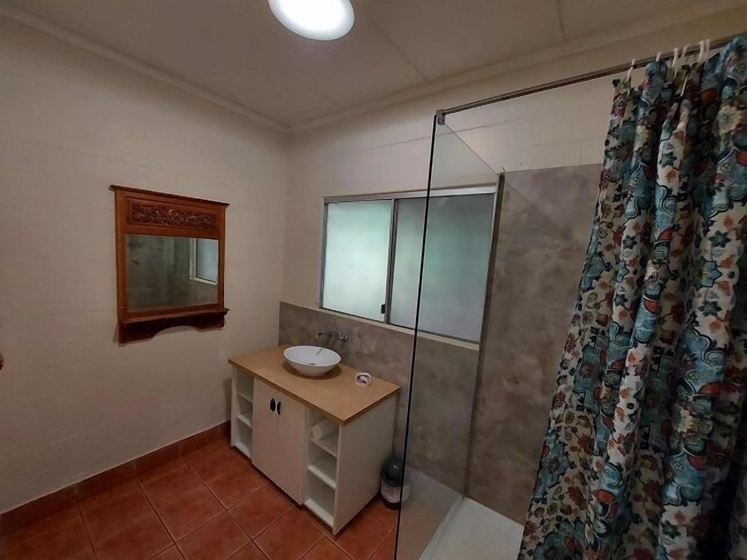 A bathroom with a wooden vanity, a mirror, a window, and a shower curtain.