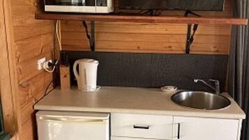 A compact kitchenette with a microwave, a small refrigerator, a sink, and a television mounted on a wooden wall.