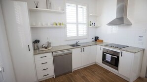 A modern kitchen with white cabinetry, a dishwasher, an oven, and a window with blinds. - Albany Central Apartments (Albany)