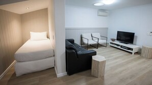 A compact room with a bed, a black sofa, a TV, and a small table. - Albany Central Apartments (Albany)