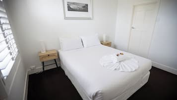 A hotel room with a bed, a bedside table, a nightstand, a framed picture on the wall, and a door.