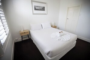 A hotel room with a bed, a bedside table, a nightstand, a framed picture on the wall, and a door.