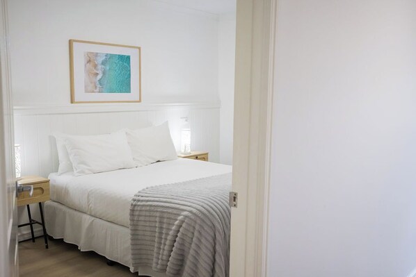 Quarto com uma cama, uma mesa de cabeceira, um quadro na parede e uma porta que dá para outro cômodo.