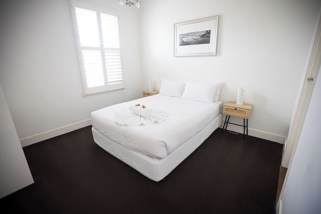 A bedroom with a bed, bedside tables, a nightstand, a framed picture on the wall, and a window.