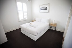 Un dormitorio con cama, mesitas de noche, una ventana y un cuadro enmarcado en la pared.