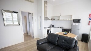 A modern kitchen with a dining table, a black leather sofa, and a white refrigerator. - Albany Central Apartments (Albany)