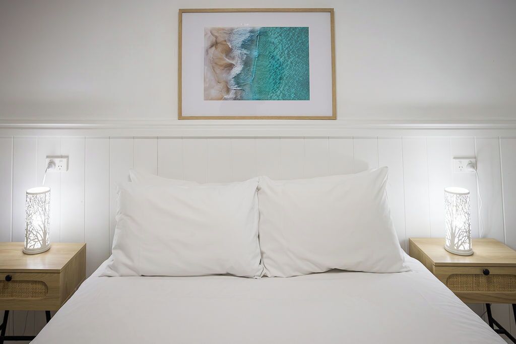A hotel room with a bed, two bedside tables, a framed picture on the wall, and two wall-mounted lamps.