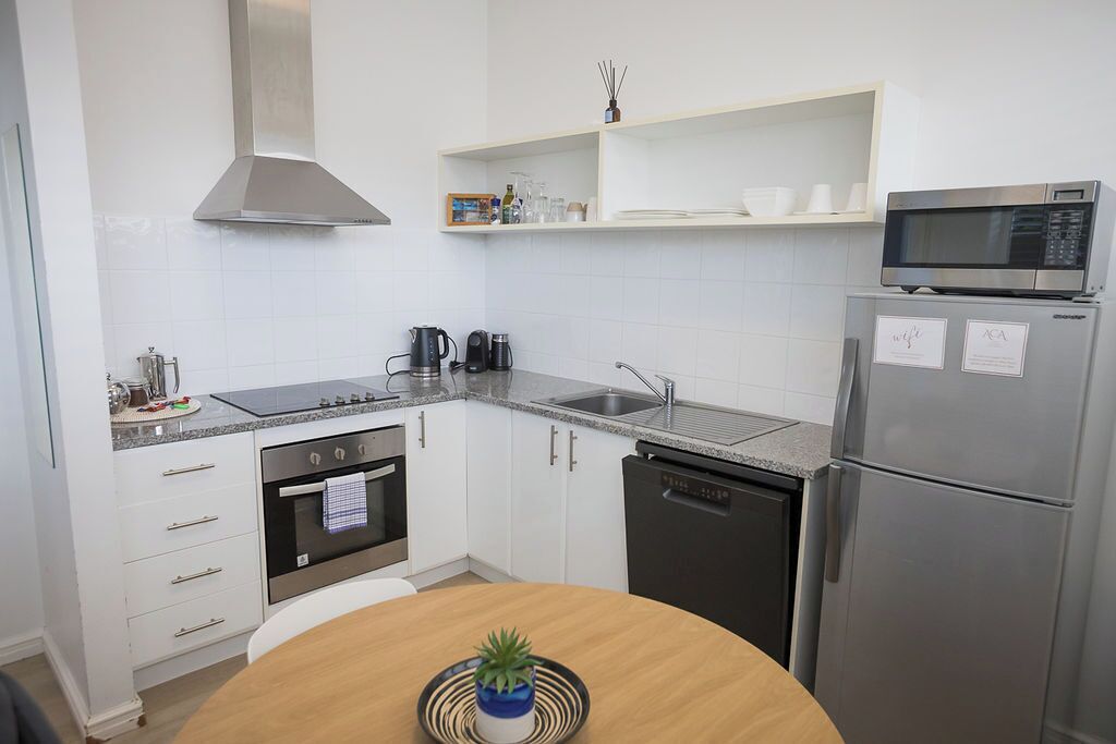 A modern kitchen with white cabinets, stainless steel appliances, and a microwave on top of a refrigerator.
