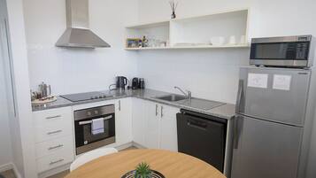 A modern kitchen with white cabinets, stainless steel appliances, and a microwave on top of a refrigerator.