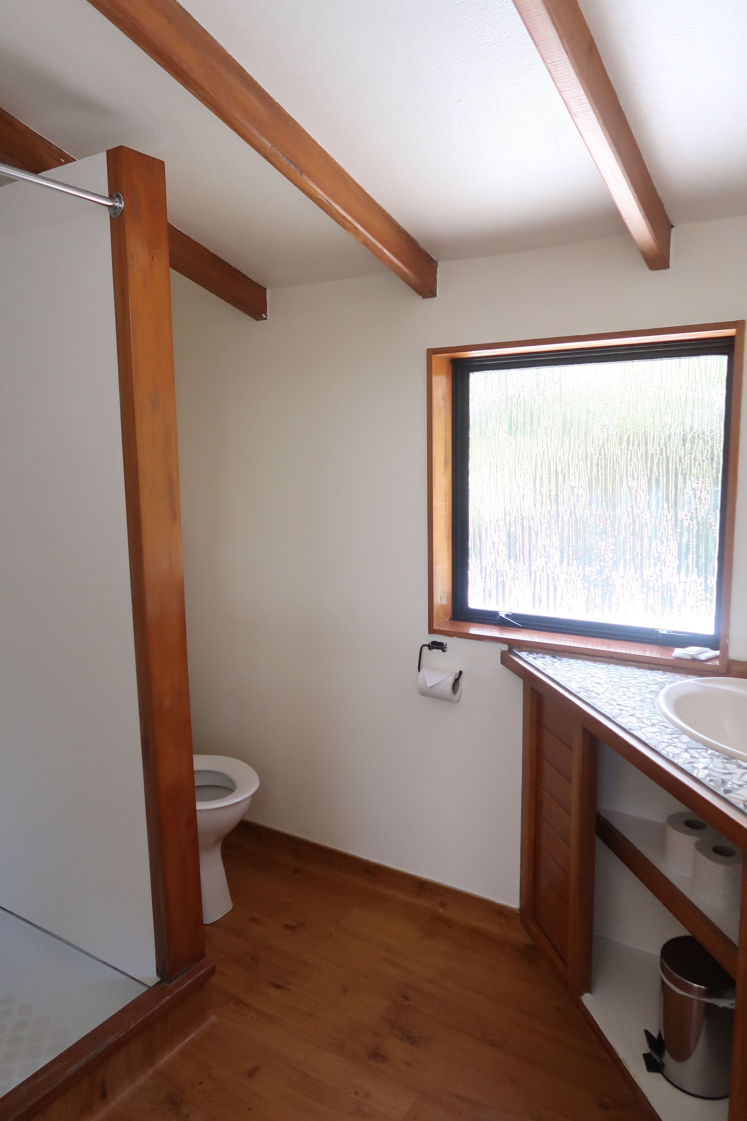 Un baño con piso de madera, un lavamanos blanco, una ventana con vistas y un inodoro.