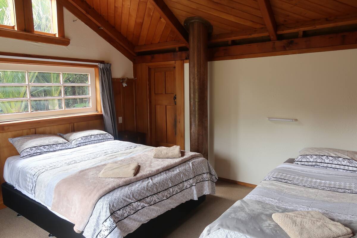 A room with two beds, wooden beams, a window with curtains, and a door.