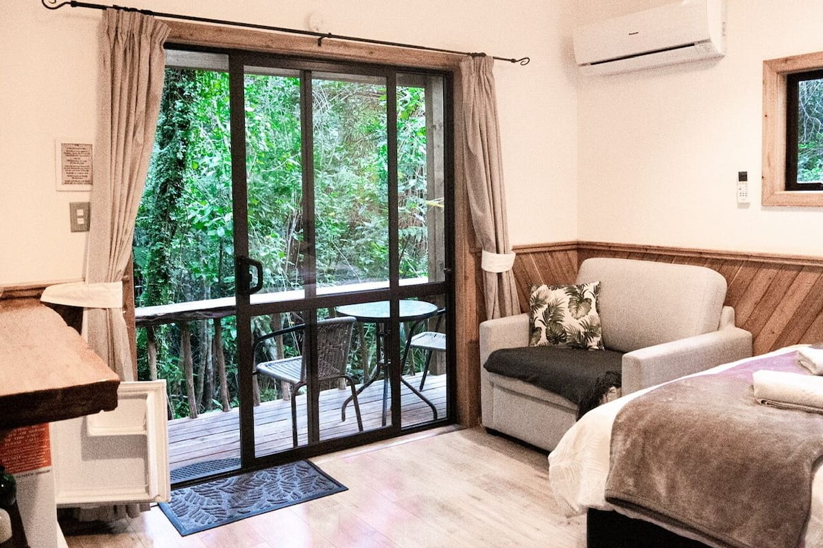 A room with a bed, a sofa, a desk, and a balcony with a table and chairs.